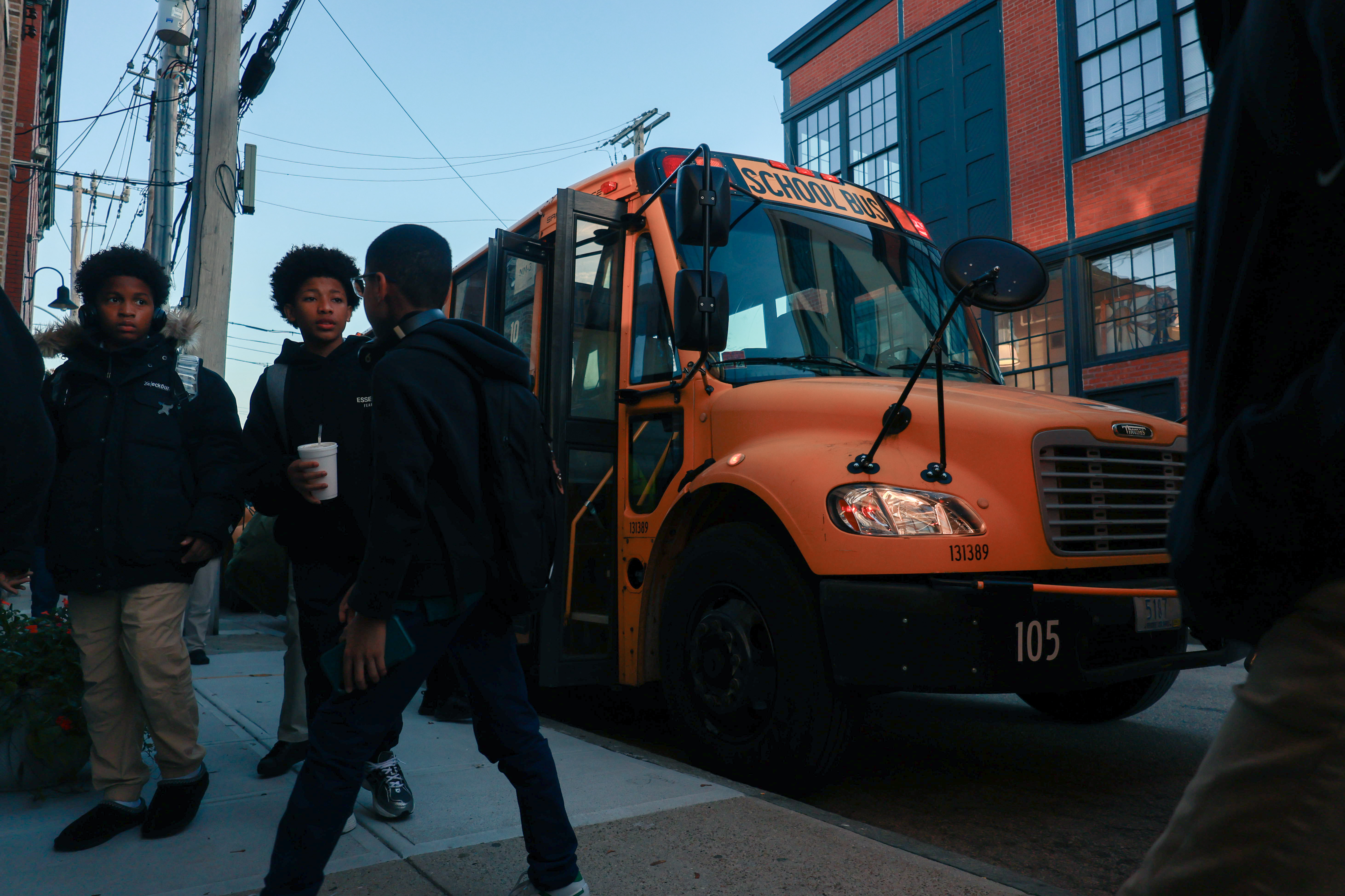 Photo of three students talking and walking together away from a yellow school bus with an open door.